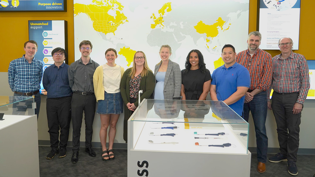 Group of people standing among display cases and against a wall of display screens. Once screen is of a map with some countries filled in with yellow. 