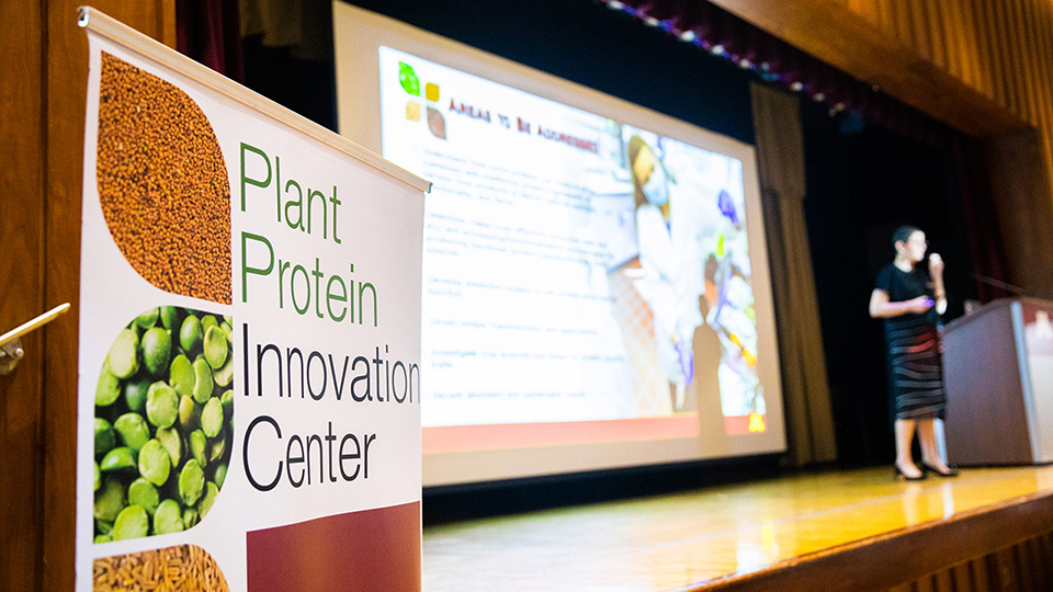 Focus on Plant Protein Innovation Center banner in front of woman on stage giving presentation