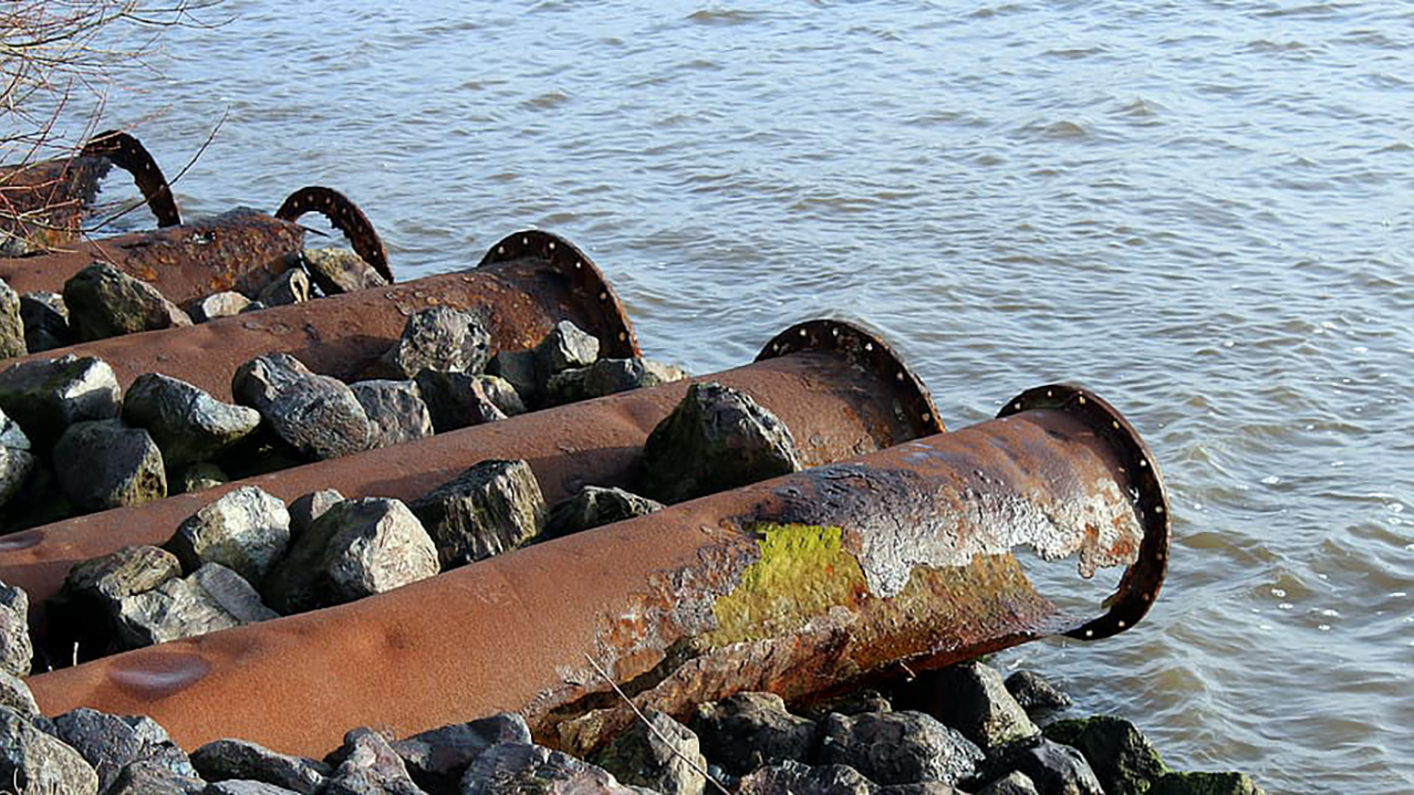 Rusting old pipes laid on a bed of rocks above a water body
