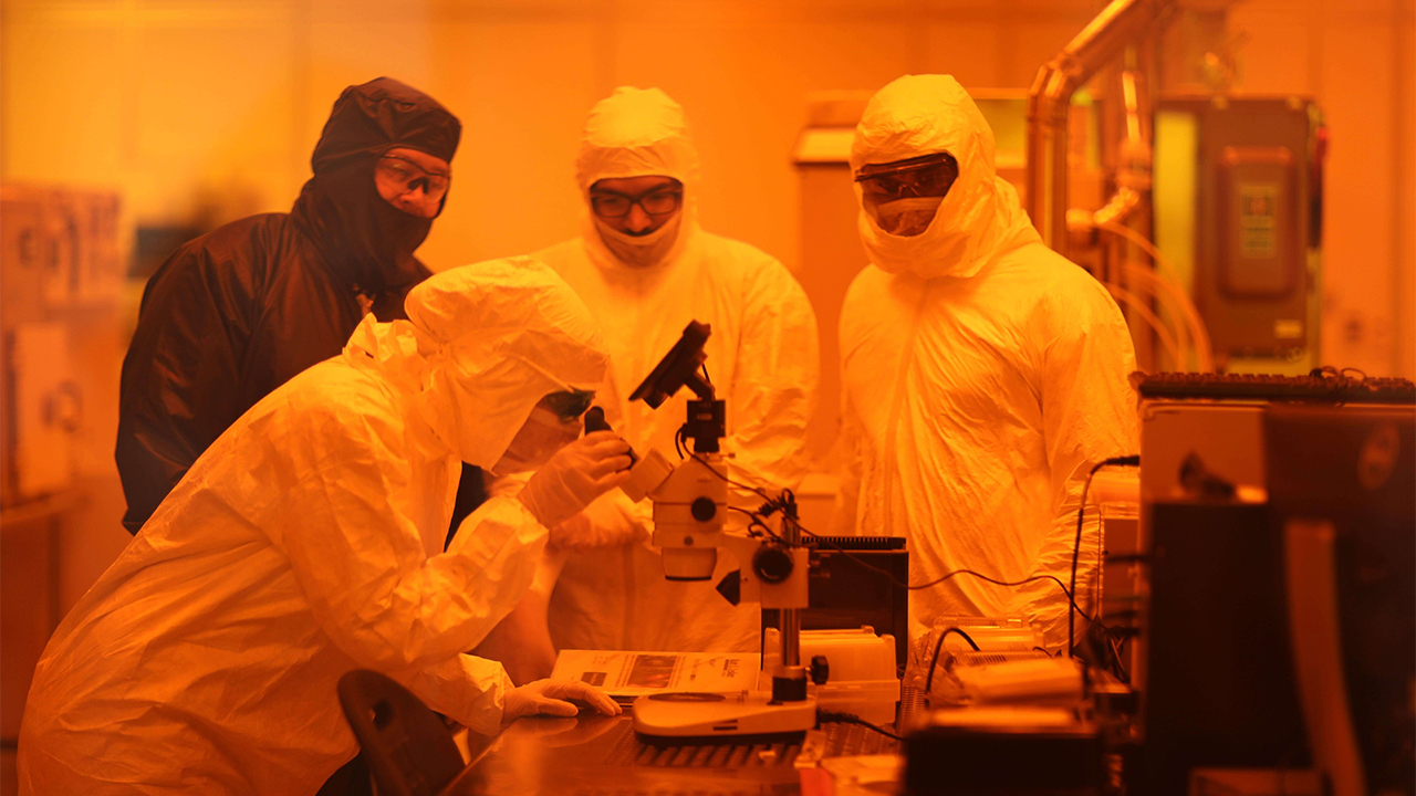 Four people in body suit PPE in an orange tinted laboratory