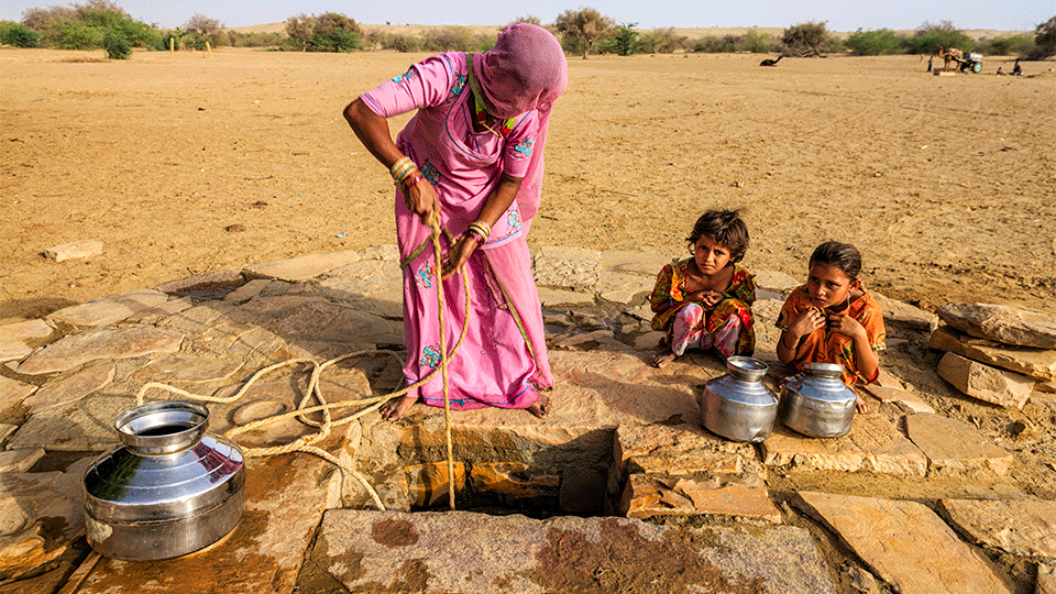 Indian woman drawing water from a well with her children looking on.