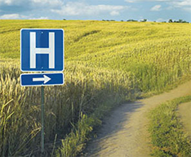 Hospital sign in middle of field by dirt road