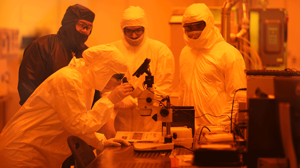 Four people in full-body PPE work around a table in a red-lit room. 