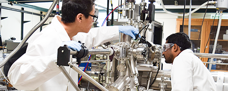 Two people in a lab, in PPE, inspecting and working with equipment