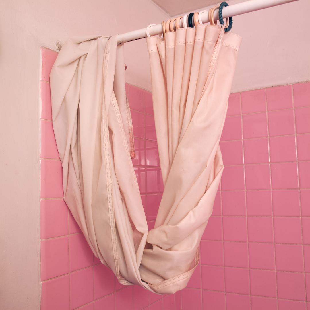 Pink shower curtain draped over a pink shower rod, in a pink tiled shower