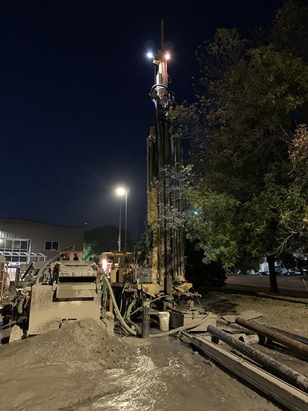 Drilling equipment shown at night at a job site where the ground is torn up