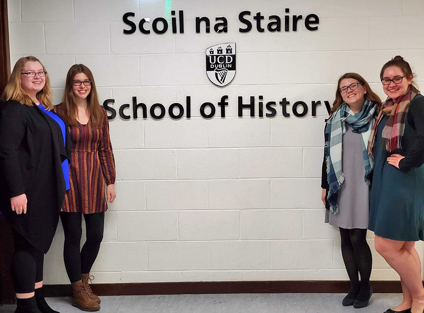 Students pose for a picture next to a sign reading "School of History"