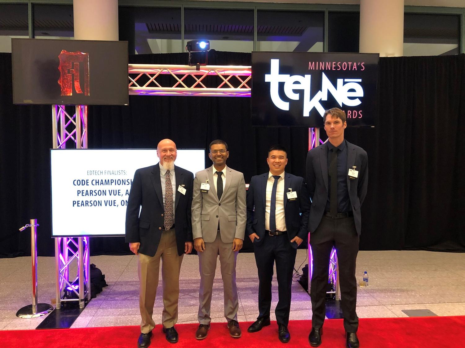 Four men in suits standing in front of a Tekne Awards red carpet picture spot