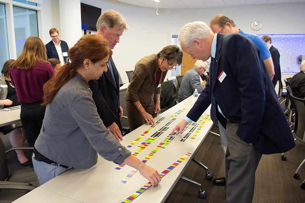 group standing at table interact with and puzzle over colorful slips of paper that representing a human genome