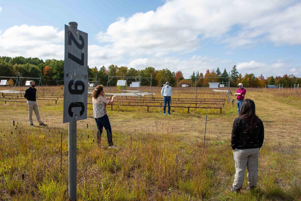 group of people stand among prairie research plots with various hardware contraptions and signs