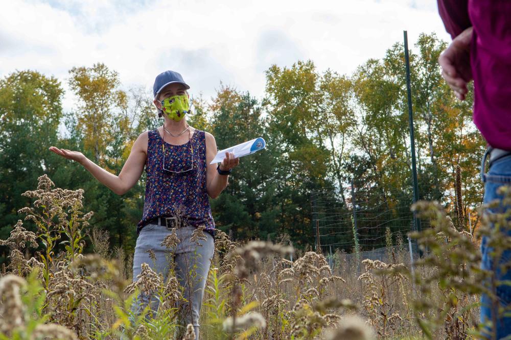 Person standing in prairie grass explaining to observers with hand gestures. 