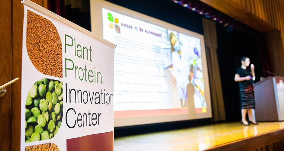 Focus on Plant Protein Innovation Center banner in front of woman on stage giving presentation
