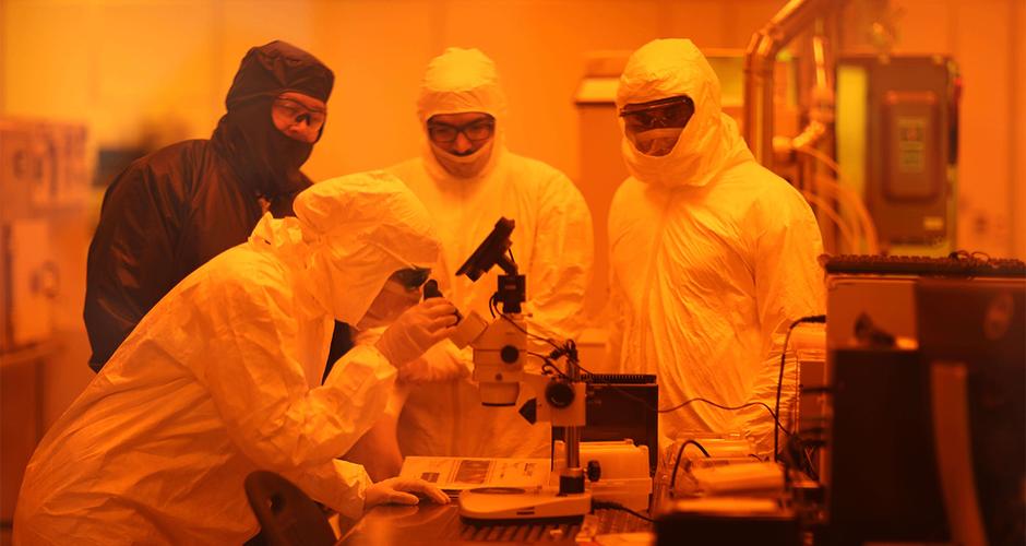 Four people in body suit PPE in an orange tinted laboratory