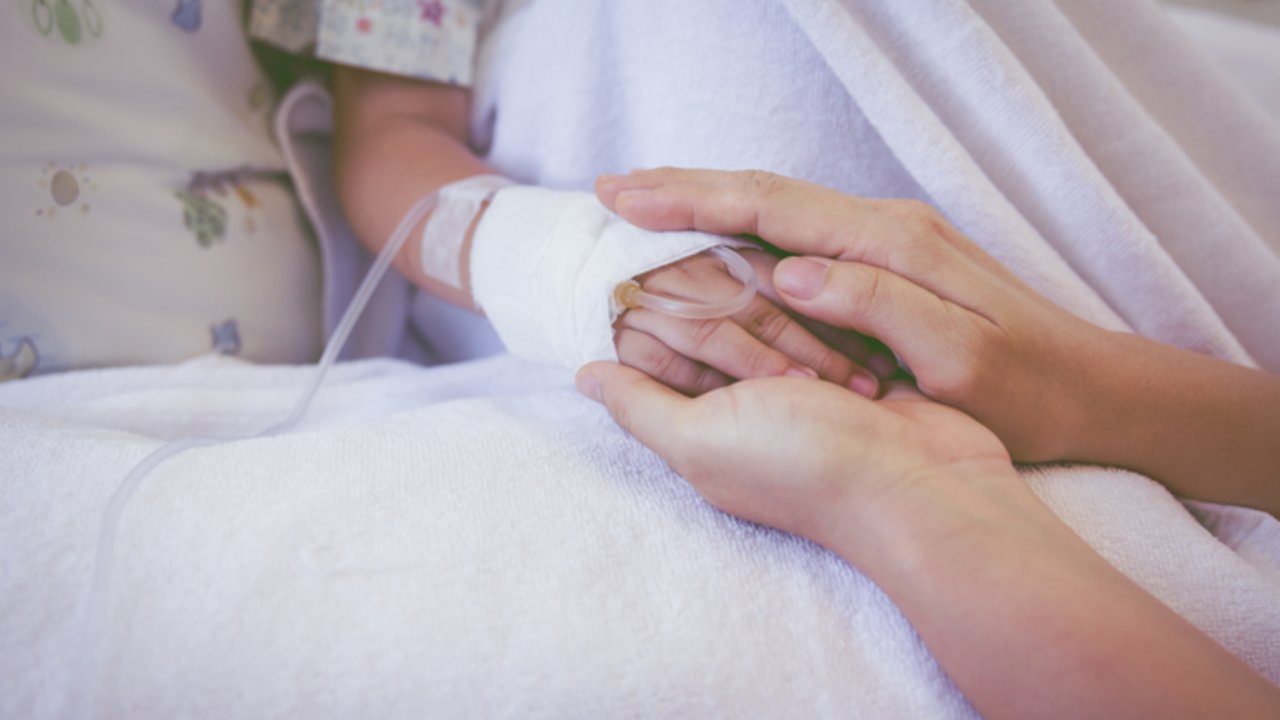 Parent holds child's hand in hospital bed