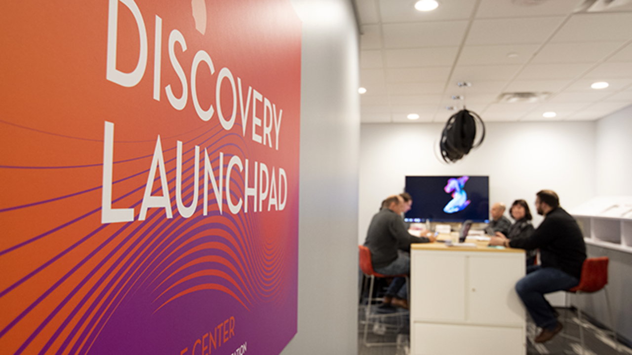 Entry to the Discovery Launchpad space, with advisers and participants sitting at a table together in the background