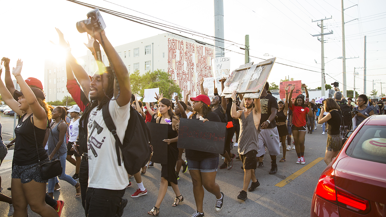 People march in protest down a street while holding signs
