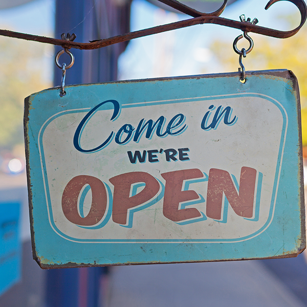 A sign reading "Come in, we're open" hangs outside of a store