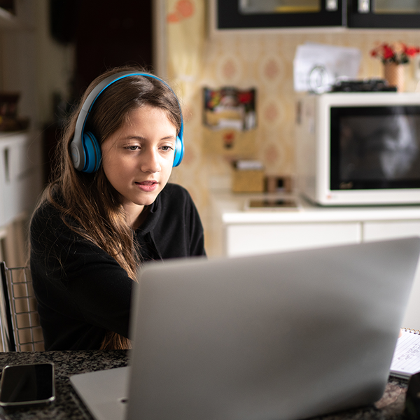Girl with headphones on doing schoolwork on a computer in at the kitchen table